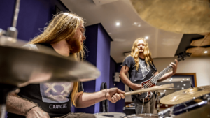 two people using the musical equipment, drums and a guitar in the Northbrook music studios