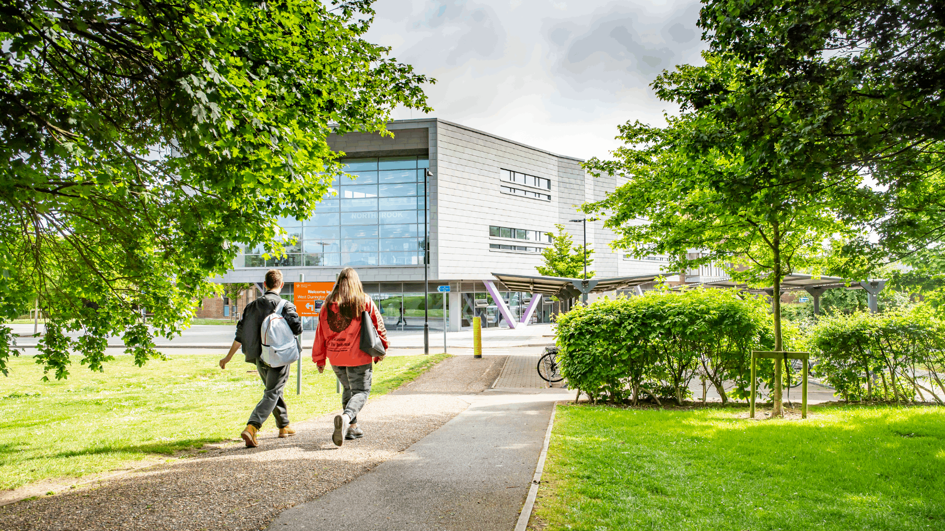A picture of the Northbrook campus on a sunny day the camera is facing towards the main building and reception. Two students walk towards the front of the campus