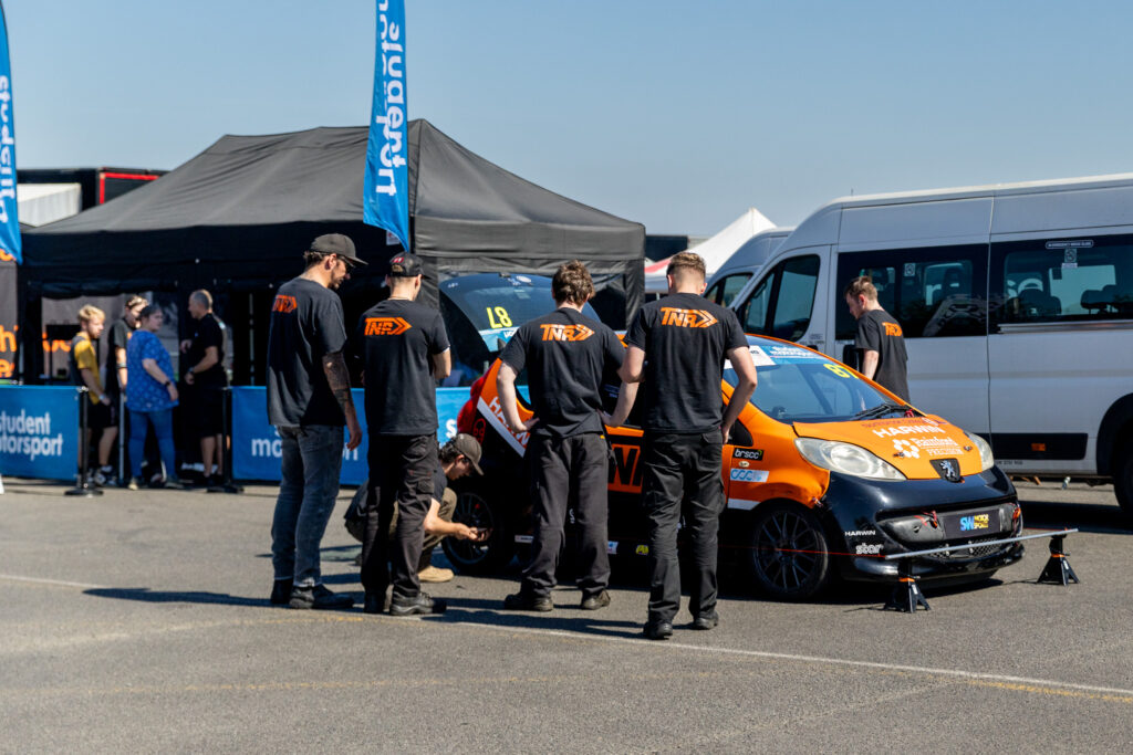 A team of students stand next to a motorsport vehicle at an event
