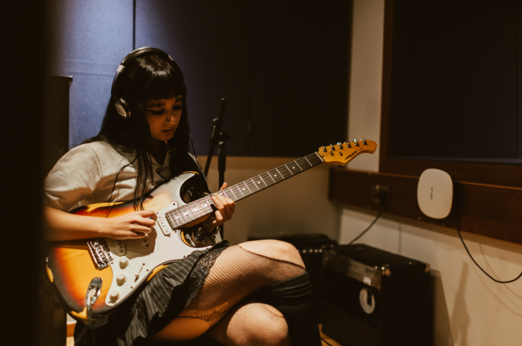 A student sat in a studio playing an electric guitar