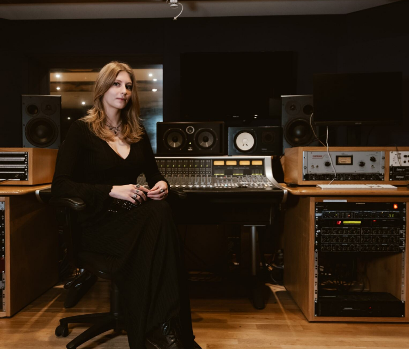 A student sits at an audio mixing booth, posing for the camera